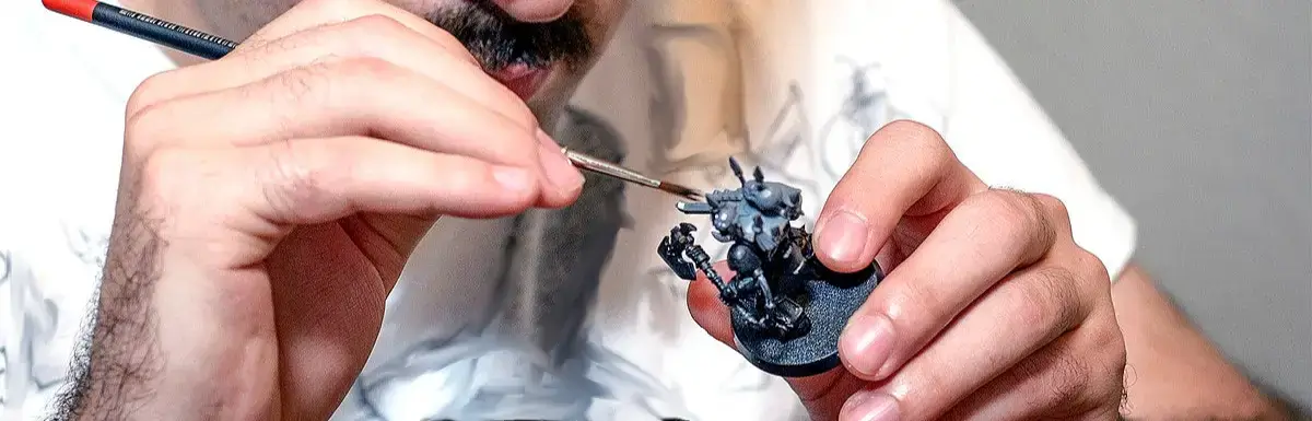 Artist painting a Warhammer 40k mini with close-up focus on hands and tools.